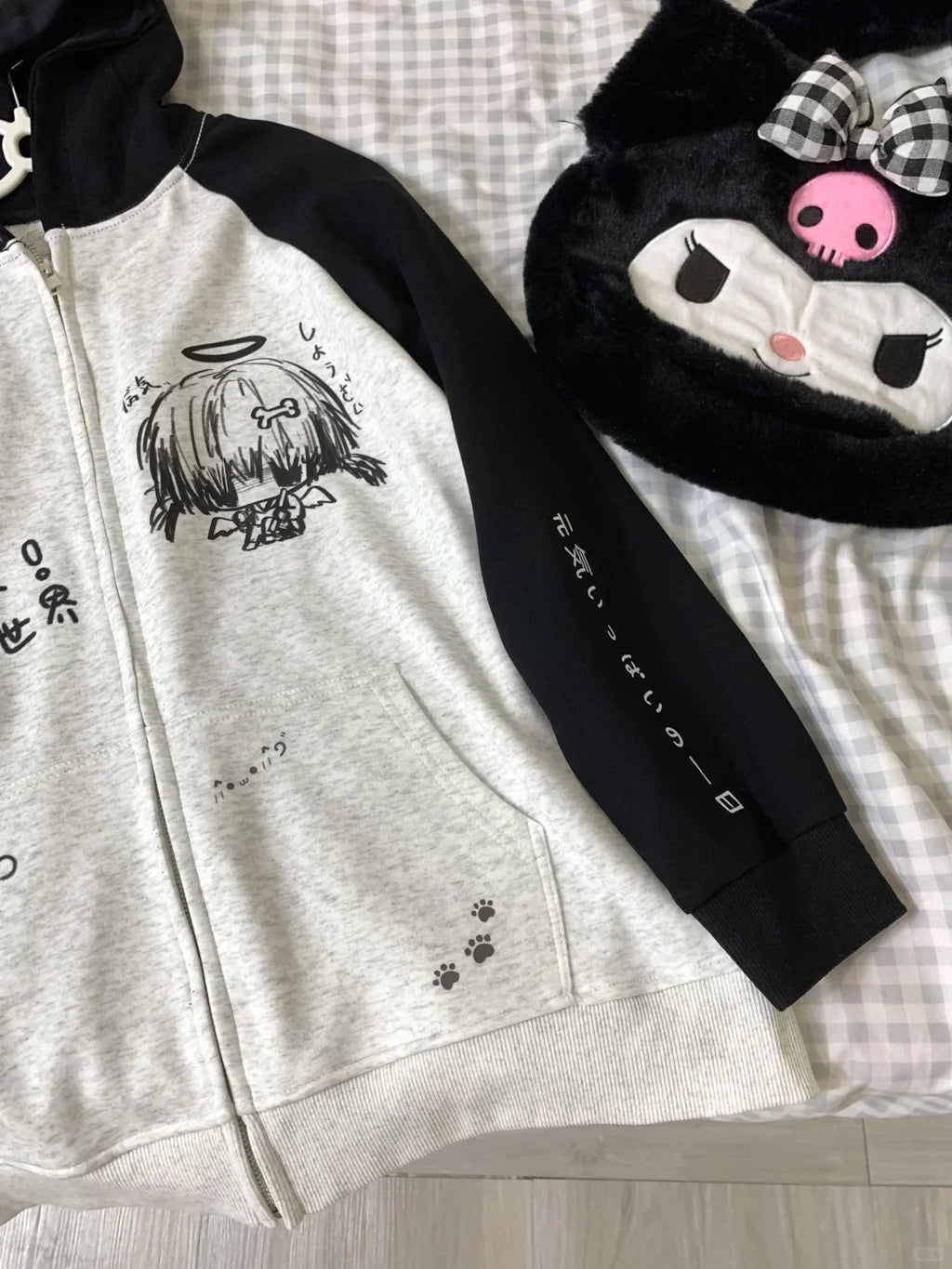 Gray hoodie with black sleeves and cartoon character design on a checkered fabric background