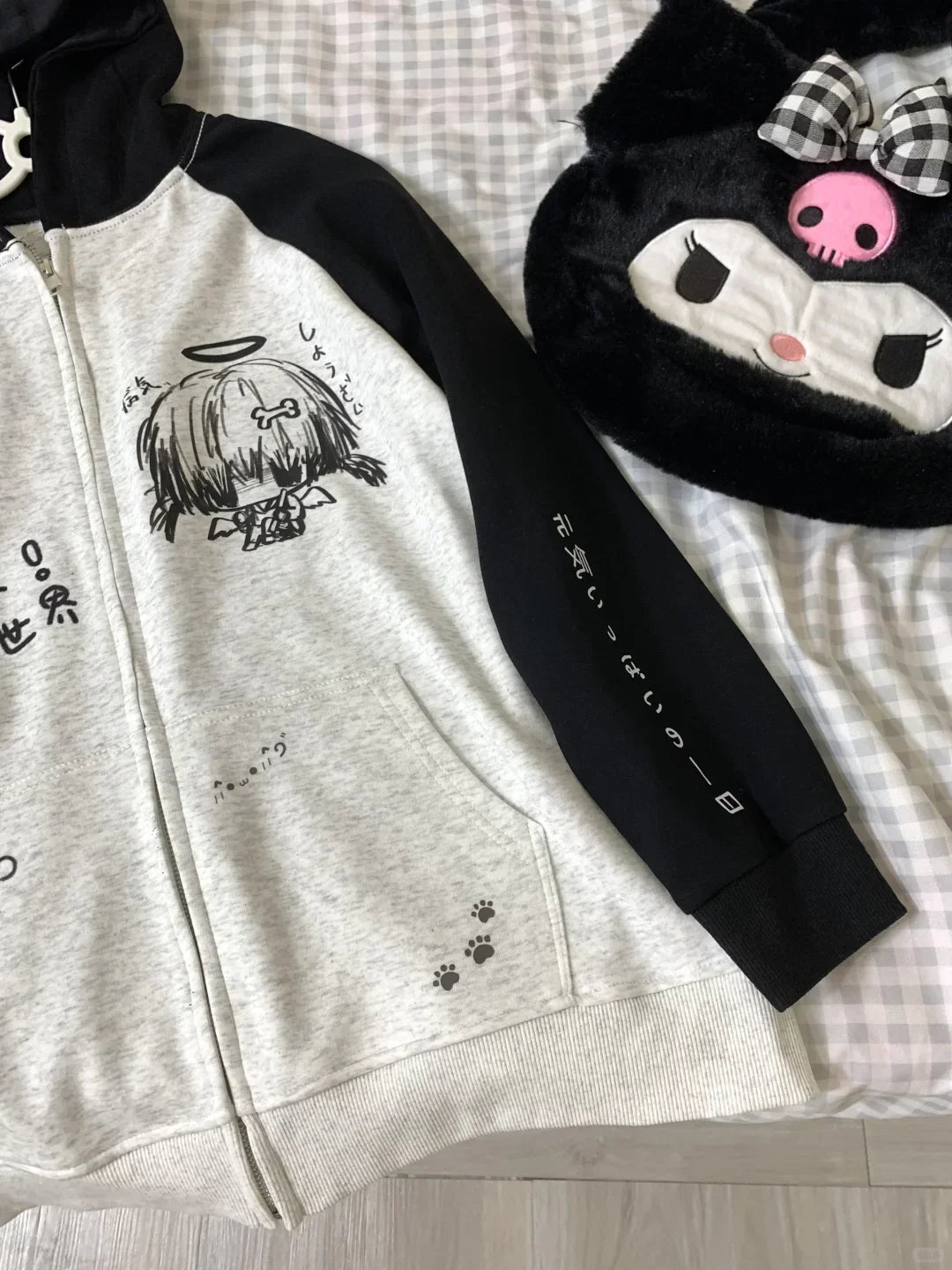 Gray hoodie with black sleeves and cartoon character design on a checkered fabric background
