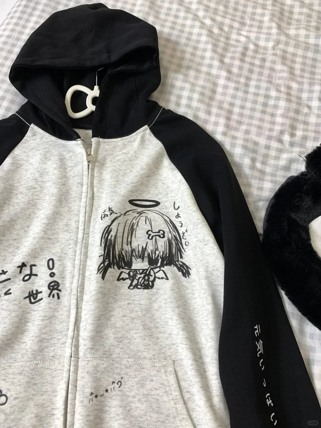Gray hoodie with black sleeves and a graphic design on a checkered fabric background