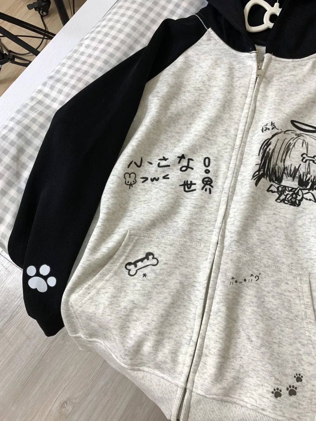Gray hoodie with black sleeves and cartoon character design on a checkered fabric background